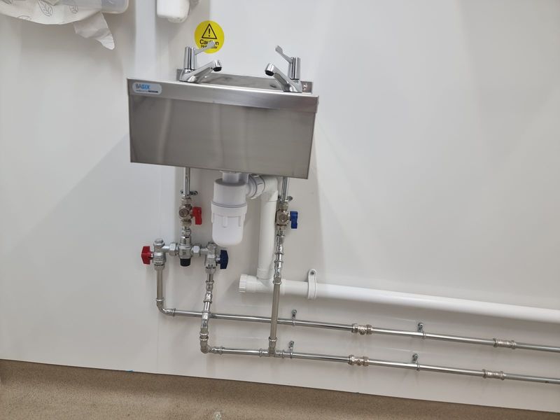 Stainless steel commercial hand wash basin with TMV mixer valve and exposed first-fix copper pipework — Smith EcoFlow commercial plumbing installation in a hotel restaurant kitchen
